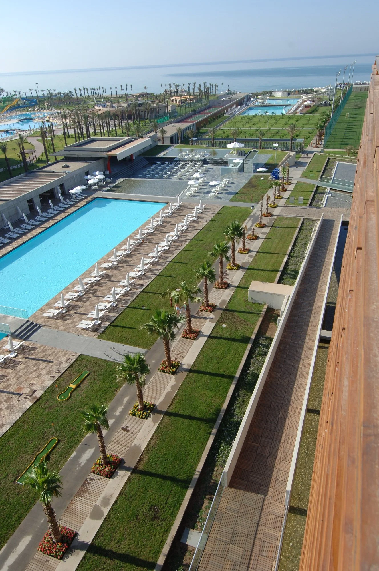 Havadan görünüm; büyük yüzme havuzları, palmiyeler ve deniz kenarında resort kompleksi